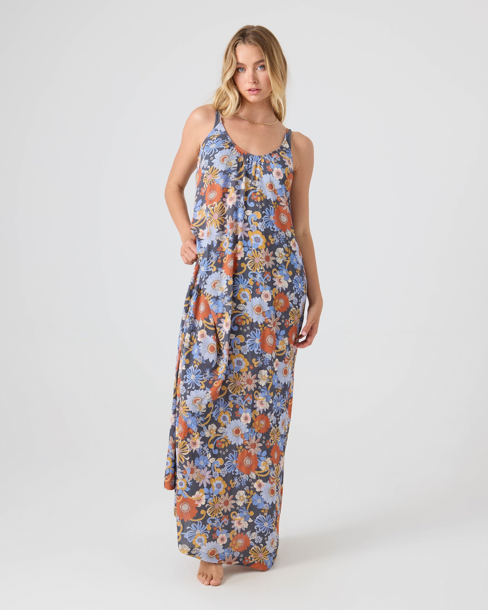 A blonde woman stands barefoot against a plain background in the Roxy®一分钟极速赛车168开奖结果记录体彩历史号码查询 Soul Flower Cover Dress—a blue, orange, and white floral maxi—holding her dress. This relaxed style is perfect as a beach cover-up.